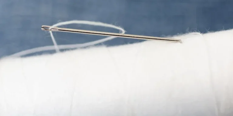 Detailed macro image of a sewing needle with white thread on a spool