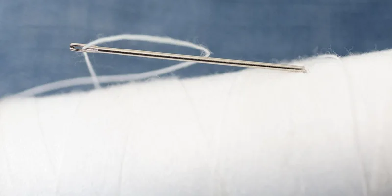Detailed macro image of a sewing needle with white thread on a spool