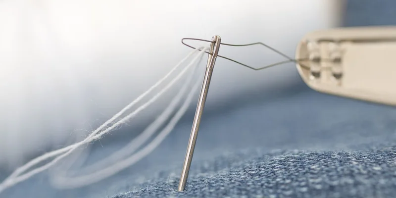 Detailed macro shot of a sewing needle threading white thread through denim fabric