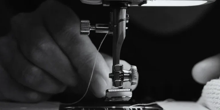 Black and white close-up of hands operating a sewing machine, threading the needle