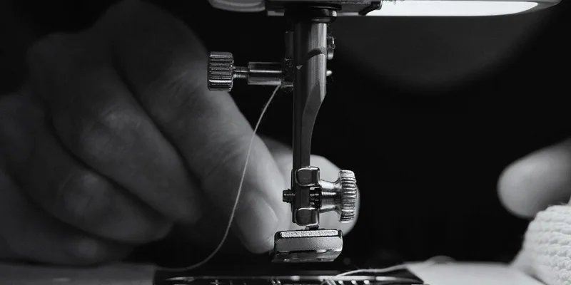 Black and white close-up of hands operating a sewing machine, threading the needle