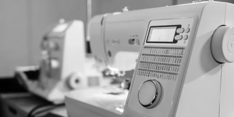 A detailed black and white close-up of a modern sewing machine showcasing its digital controls and patterns