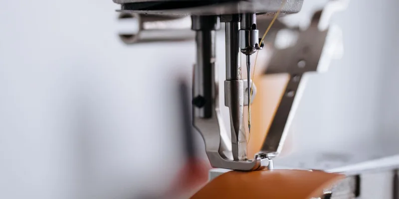 Detailed shot of a sewing machine's needle and presser foot working on leather material