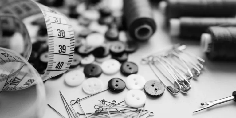 Black and white sewing materials including buttons, needles, and thread spools on a white surface