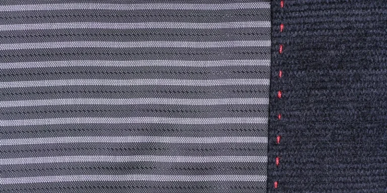 Detailed close-up of striped fabric featuring contrasting red stitching along the edge