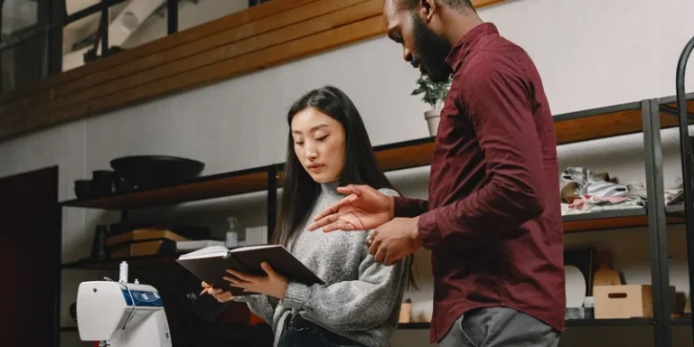 Two designers discussing garment creation in a fashion studio with a sewing machine and fabric