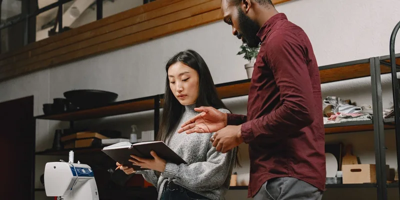 Two designers discussing garment creation in a fashion studio with a sewing machine and fabric