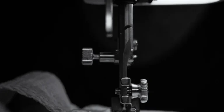 Close-up of sewing machine needle stitching beige fabric in black and white