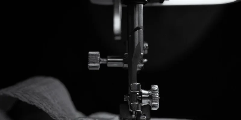 Close-up of sewing machine needle stitching beige fabric in black and white