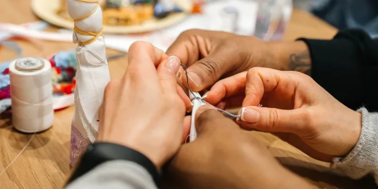 Hands sewing with a needle and thread in a close-up view on a wooden table
