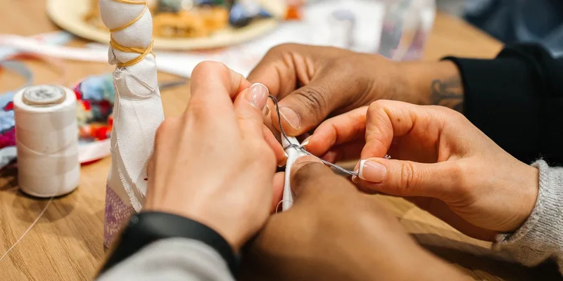 Hands sewing with a needle and thread in a close-up view on a wooden table