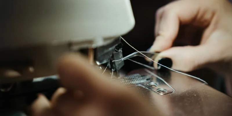 A close-up of hands threading a sewing machine in a workshop setting